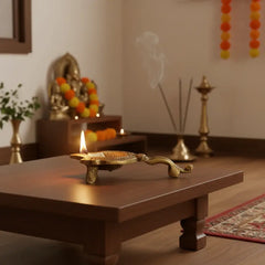 Close-up of a golden brass aarti diya with a handle, featuring an Om symbol embossed in the center of the oil lamp bowl.