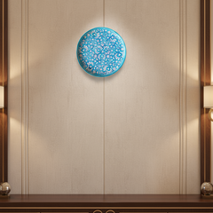 A round decorative wall plate with an intricate hand-painted white floral and vine pattern on a vibrant turquoise background.