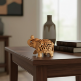 A light-colored wooden elephant figurine with its trunk raised, featuring detailed filigree carving and cut-out patterns on its body and back.