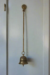 Decorative metal bell hanging in a sunlit room with intricate ceiling designs.