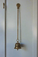 Decorative metal bell hanging in a sunlit room with intricate ceiling designs.