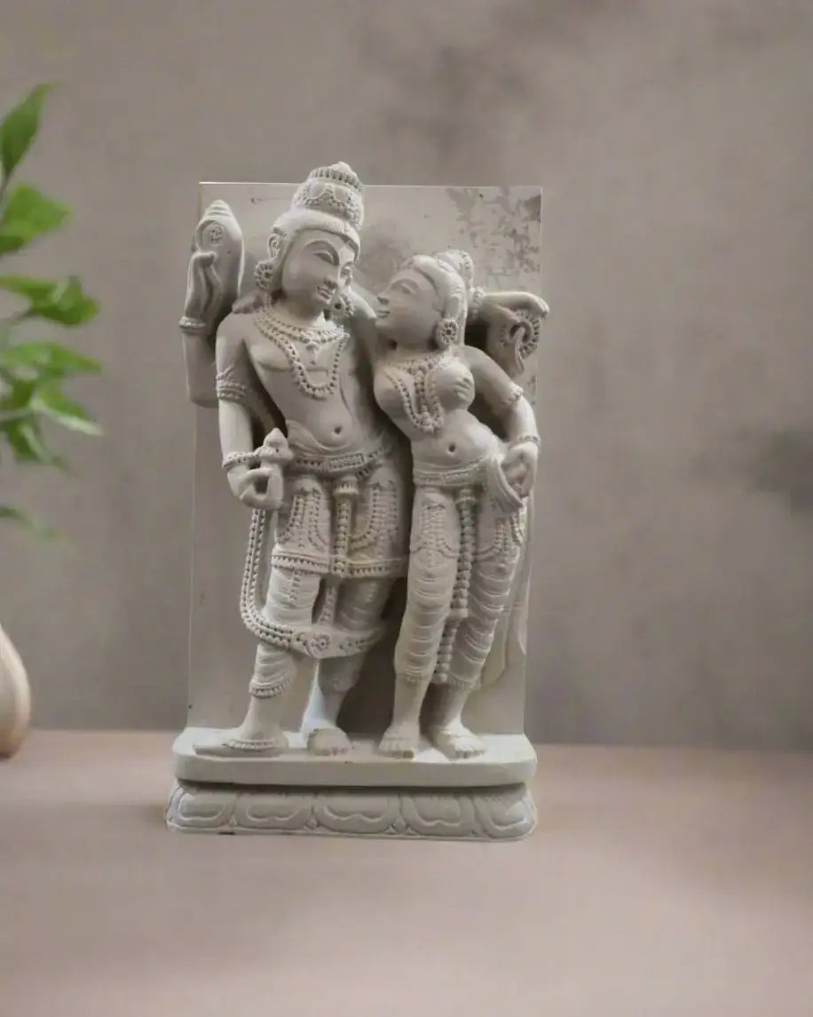 Decorative stone sculpture of two figures outdoors with plants in the background