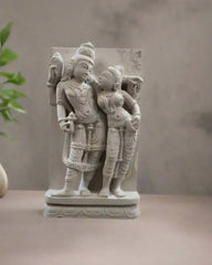 Decorative stone sculpture of two figures outdoors with plants in the background