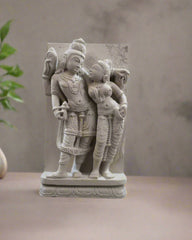 Decorative stone sculpture of two figures outdoors with plants in the background