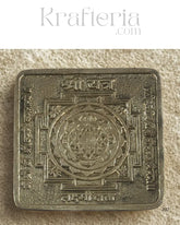Decorative metal square with intricate designs on a textured beige background