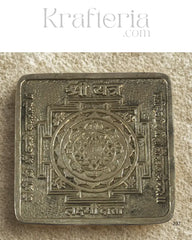 Decorative metal square with intricate designs on a textured beige background