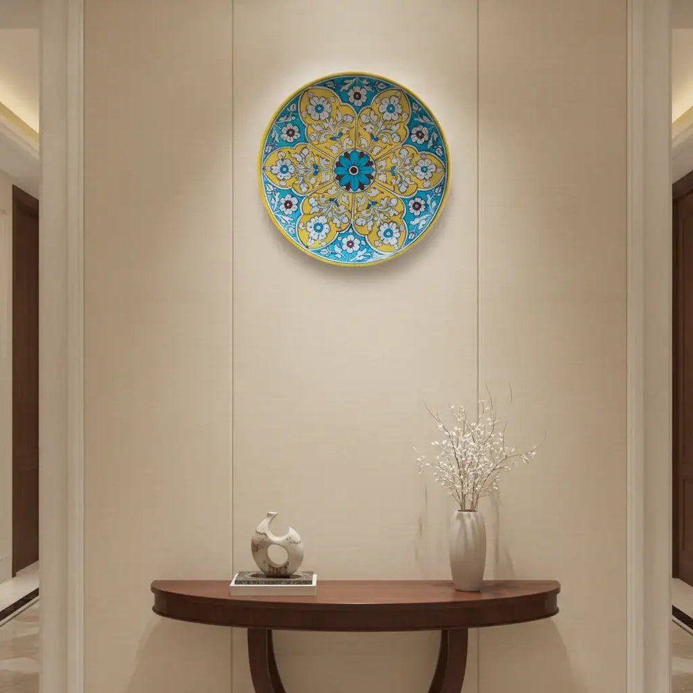 A round decorative wall plate with a vibrant yellow and teal floral medallion pattern, featuring white floral details and a central teal and maroon flower, framed by a yellow rim.