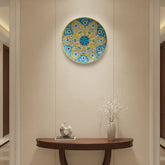 A round decorative wall plate with a vibrant yellow and teal floral medallion pattern, featuring white floral details and a central teal and maroon flower, framed by a yellow rim.