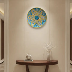 A round decorative wall plate with a vibrant yellow and teal floral medallion pattern, featuring white floral details and a central teal and maroon flower, framed by a yellow rim.