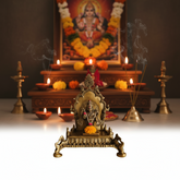 An ornate brass Singhasan (throne) for deity idols, featuring intricate carvings, a central floral design, and bird figures, on a white surface.