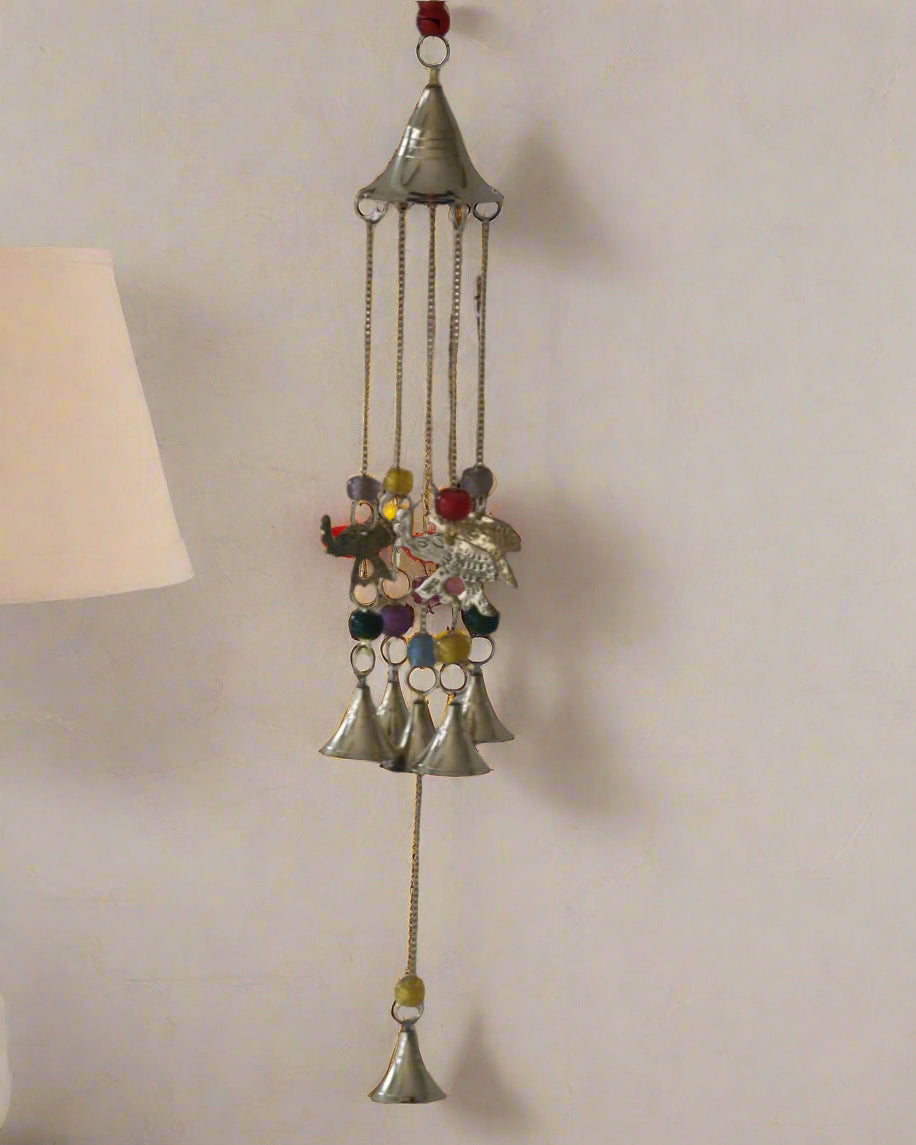 Decorative wind chime with colorful stones and bells on a plain wall.