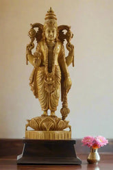 Gold-colored statue in a decorative indoor setting with plants and architectural elements.