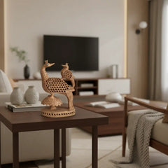 A hand-carved light wooden figurine depicting two peacocks, one large and one small, with intricate filigree cut-out patterns on their bodies and small blue eye accents, all on a decorative base.
