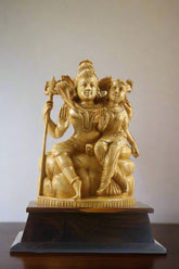 Gold-colored statue of a seated figure with another figure on a wooden base, displayed indoors.