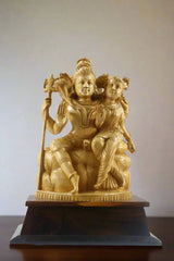 Gold-colored statue of a seated figure with another figure on a wooden base, displayed indoors.