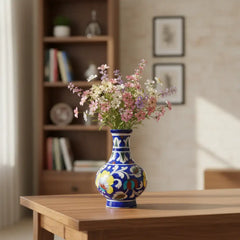 A blue pottery vase with a bulbous base and slender neck, intricately hand-painted with vibrant multi-colored floral designs in yellow, red, and light blue against a dark blue background, isolated on white.