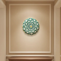A decorative wall plate with a pattern of green leaves, small red dots, and yellow dots arranged around a yellow and blue starburst center, with a scalloped edge.