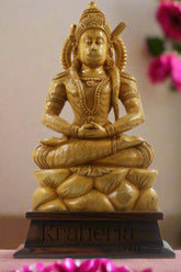 Gold-colored statue of a seated figure on a wooden base with a textured wall background