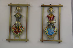 Two decorative wall hangings with colorful figures in gold frames on a white wall.