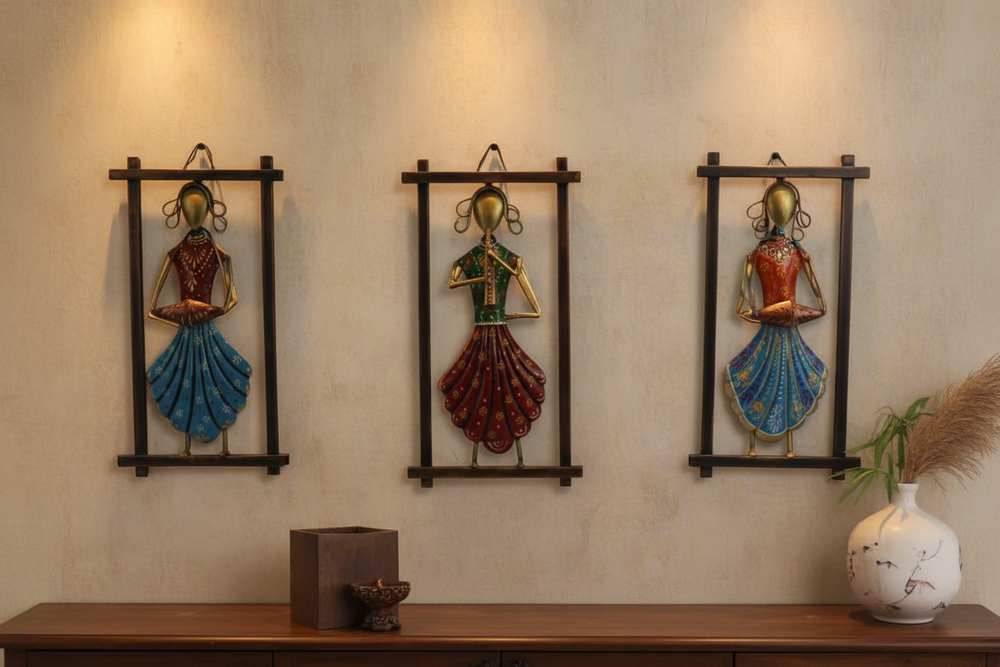 Three decorative wall hangings of women in colorful outfits on a beige wall.