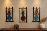 Three decorative wall hangings of women in colorful outfits on a beige wall.