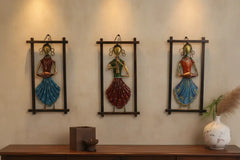 Three decorative wall hangings of women in colorful outfits on a beige wall.