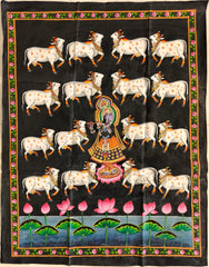 A traditional Indian Pichwai painting on a black background, depicting Lord Krishna (Shrinathji) playing a flute, surrounded by white cows, and a pond with pink lotus flowers at the bottom. The painting has a decorative border.