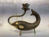 An artistic brass oil lamp shaped like a fish with detailed scales, whose curved body acts as a stand for a lotus-shaped lamp cup extending from its head.