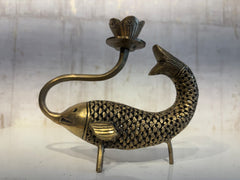 An artistic brass oil lamp shaped like a fish with detailed scales, whose curved body acts as a stand for a lotus-shaped lamp cup extending from its head.