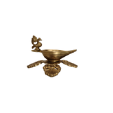 Side view of a handcrafted brass peacock diya oil lamp with an ornate four-pointed base, on a white background.
