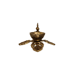 Side view of a handcrafted brass peacock diya oil lamp with an ornate four-pointed base, on a white background.
