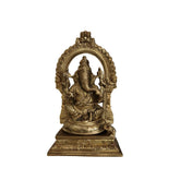 Golden brass Ganesha idol with an elaborate arch behind, sitting on a base, against a white background.