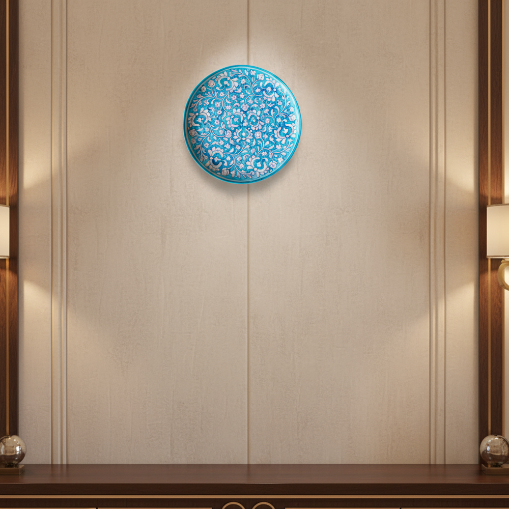 A round decorative wall plate with an intricate hand-painted white floral and vine pattern on a vibrant turquoise background.