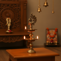 A tall, golden brass multi-tier oil lamp with two levels of deepak bowls and an ornate peacock figurine at the very top, against a light, textured background.