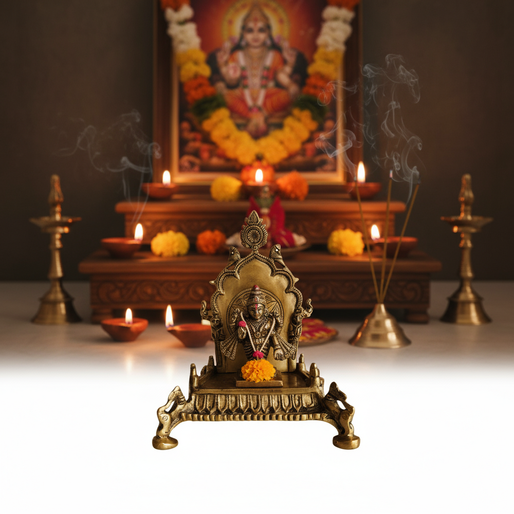 An ornate brass Singhasan (throne) for deity idols, featuring intricate carvings, a central floral design, and bird figures, on a white surface.