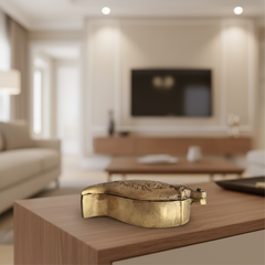 Top-down view of a small, ornate brass box in a mango or paisley shape, featuring detailed floral engravings and a small clasp/handle at one end, on a white surface.