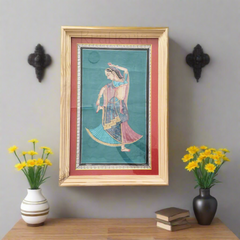 Framed artwork of a dancer on a wall with two vases and books on a table below.