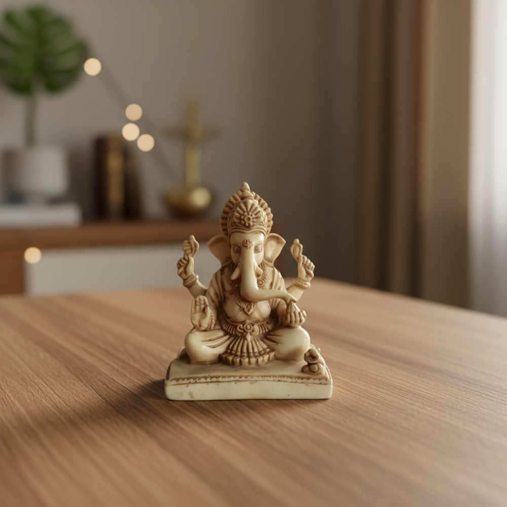 A light-colored resin statue of Lord Ganesha seated, with intricate details on his crown, robes, and four arms holding symbols, and his mouse vehicle at his feet.