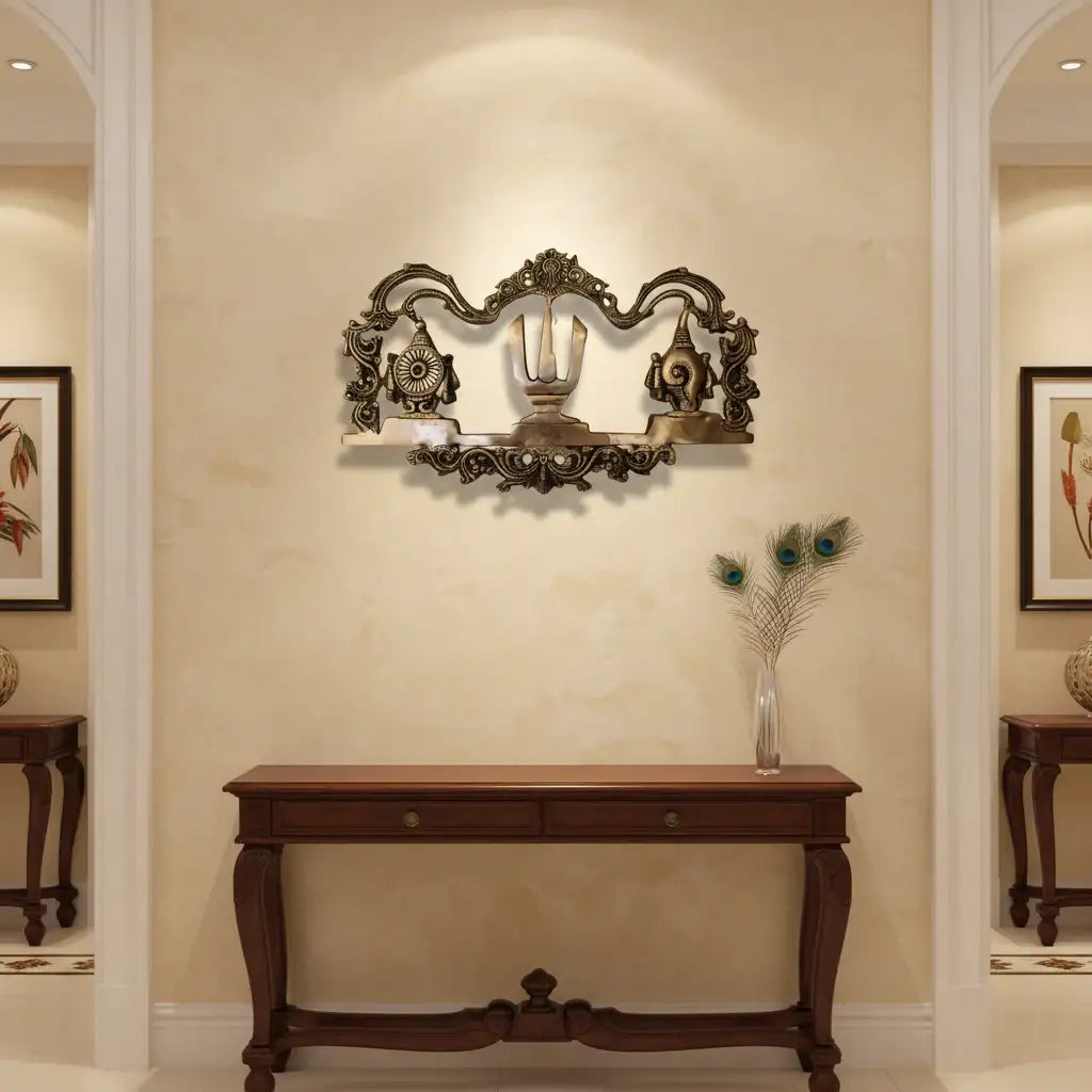 An ornate brass wall hanging displaying the U-shaped Venkateswara Namam (tilak) in the center, flanked by the Shankha (conch) and Chakra (discus) symbols, with decorative border work.