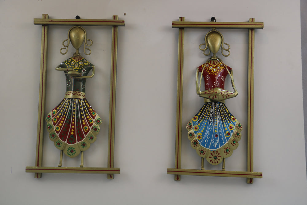 Two decorative wall hangings with colorful figures in gold frames on a white wall.