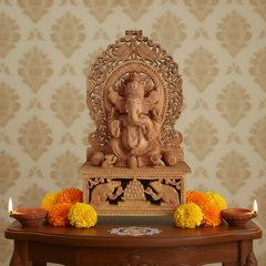 Carved wooden deity statue on a table with marigold flowers and oil lamps against a patterned wall.