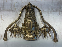 A detailed brass wall hanging depicting the face of Lord Venkateswara, adorned with a tall crown, traditional markings, and flanked by symbolic conch and discus motifs.