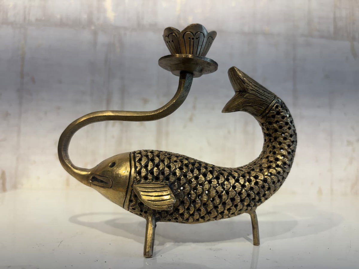 An artistic brass oil lamp shaped like a fish with detailed scales, whose curved body acts as a stand for a lotus-shaped lamp cup extending from its head.