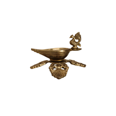 Side view of a handcrafted brass peacock diya oil lamp with an ornate four-pointed base, on a white background.