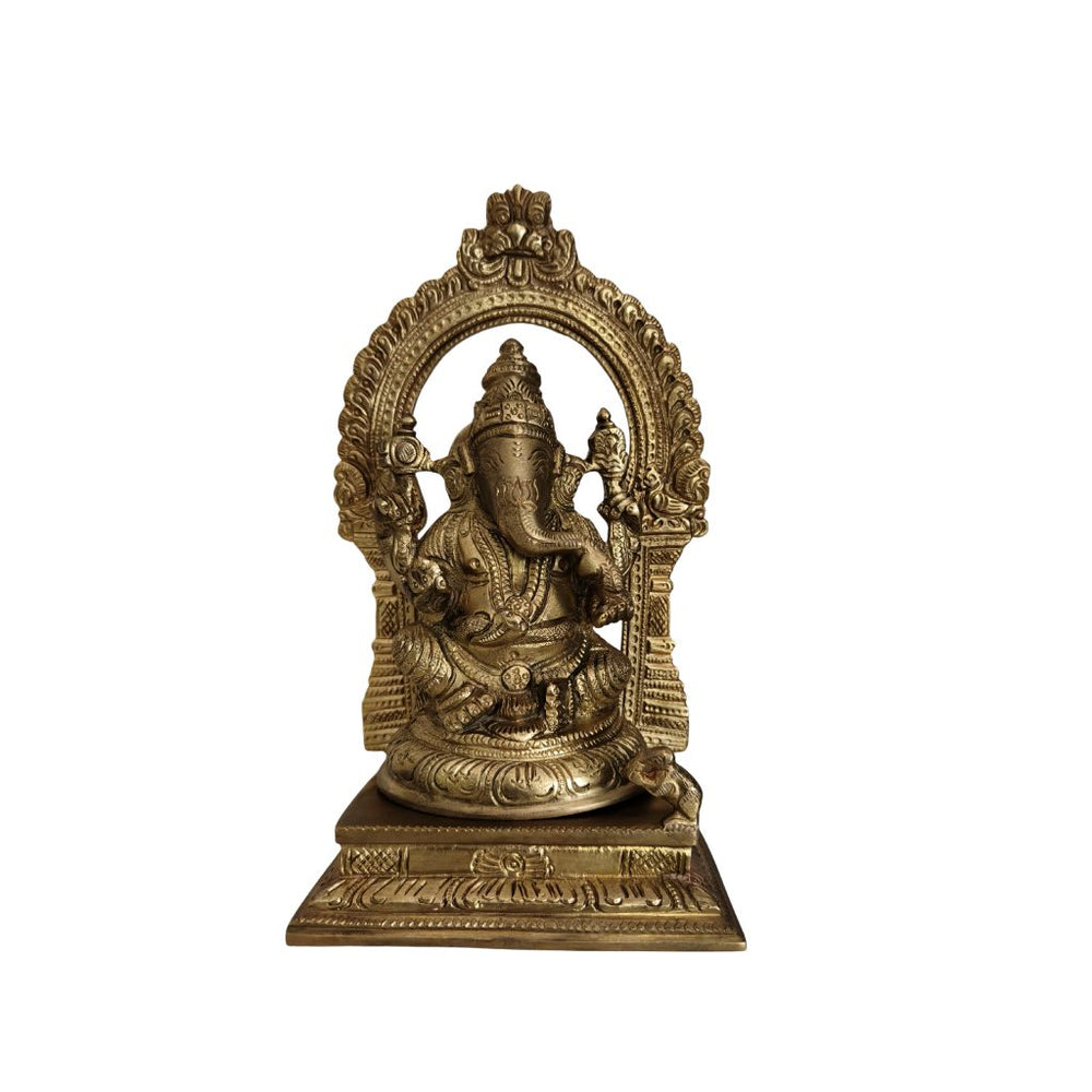 Golden brass Ganesha idol with an elaborate arch behind, sitting on a base, against a white background.